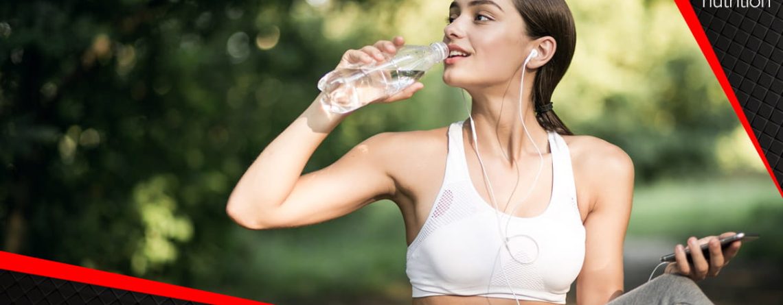 Hidratacija tijekom ljetnih vrućina – žena u sportskoj odjeći pije vodu na otvorenom, naglašavajući važnost unosa tekućine i elektrolita.